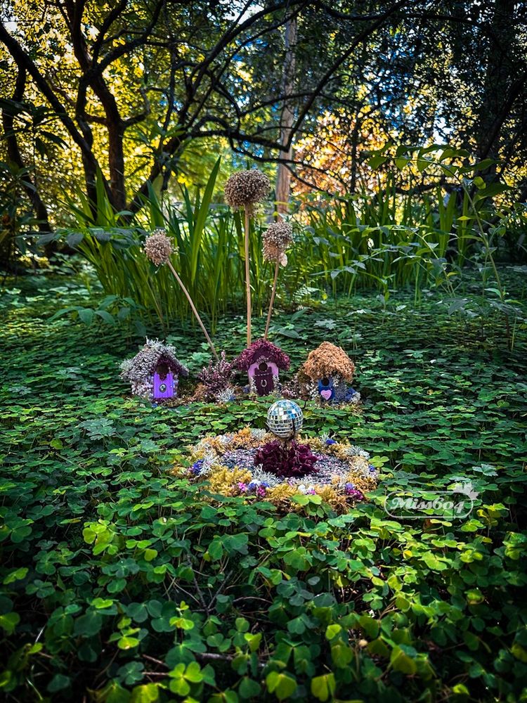 Sitting on top of a garden covered in vines, little fairy houses made of flowers and plants including a tiny dance floor with flower petals and a disco ball 