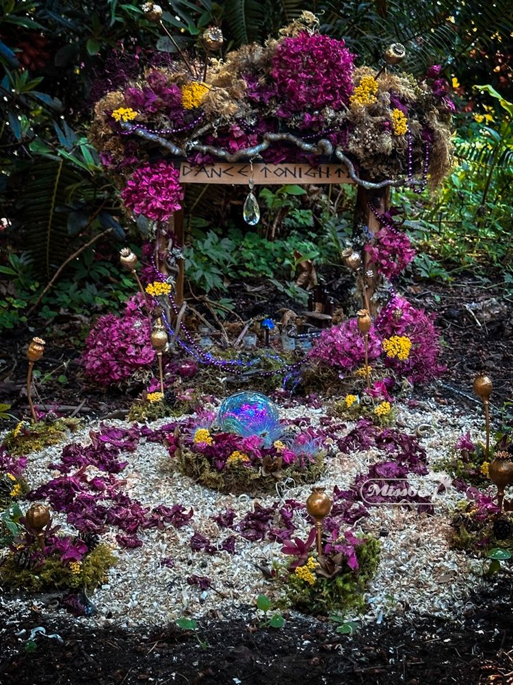 In the garden, flower petals are arranged in a circle and around a mini archway with a sign “Dance Tonight” ready for a little fairy party 