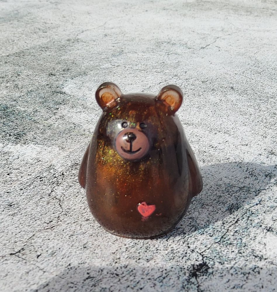 Round bear figurine made from brown resin with mica powder. The face details and a red heart on his lower body have been painted on with acrylic markers