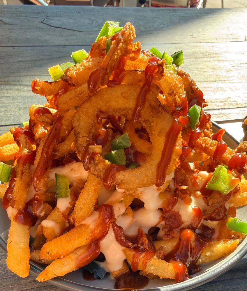 Pile of crispy fries with garlic butter and seasoning topped with Queso + Raw Jalapeno + Onion Tanglers + BBQ Sauce
