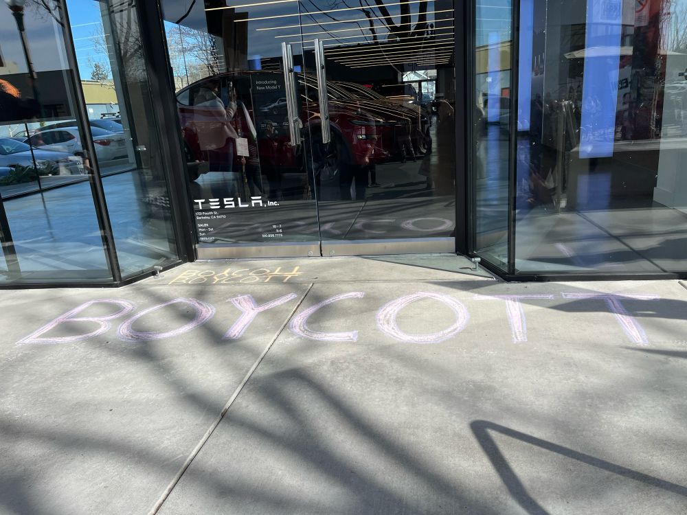 “BOYCOTT” written in chalk on the pavement in front of the Tesla showroom in Berkeley, CA.
