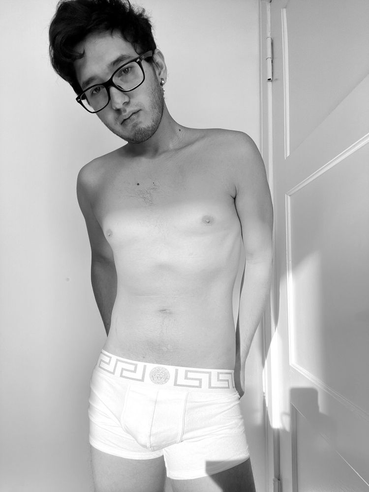 A black and white photo of a twink with glasses in Versace boxer briefs