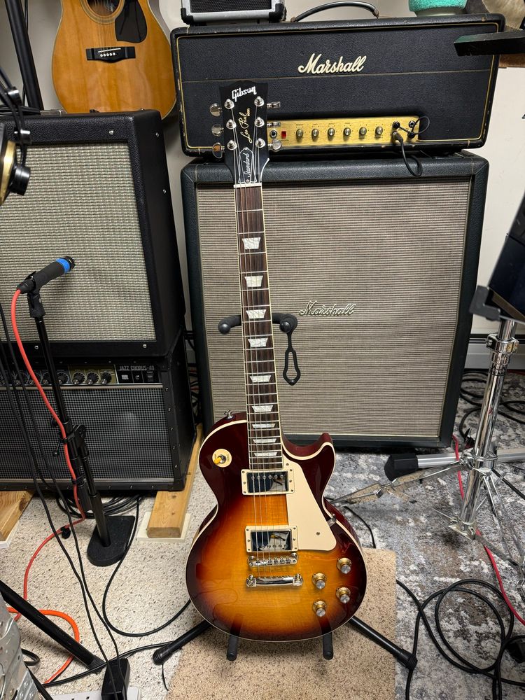 A music studio with a guitar on a stand sitting in front of a large speaker cabinet and amp head. 