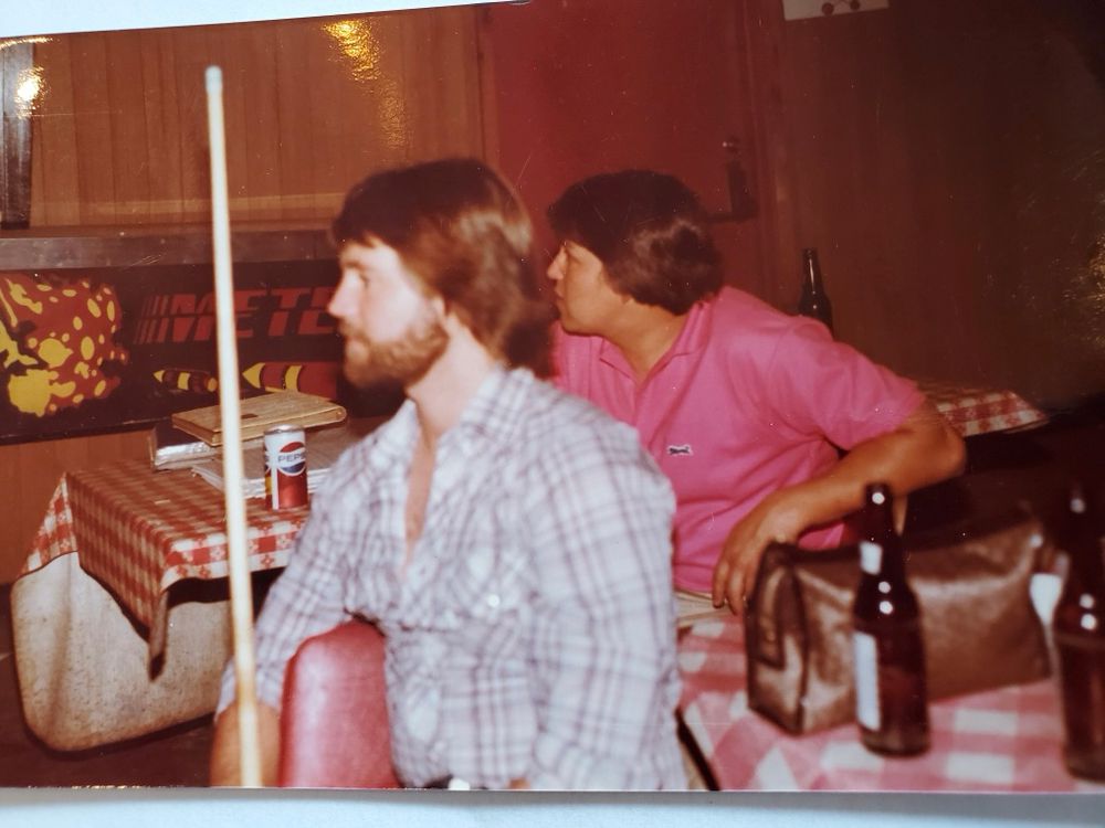 Another angle. My uncle sitting at a table. A bearded man seated closer to the camera 
