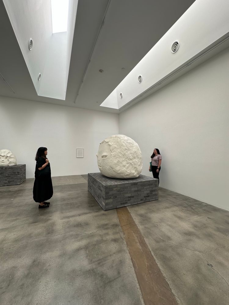 Two people standing around yoshimoto Nara’s giant head sculpture just like in his drawing