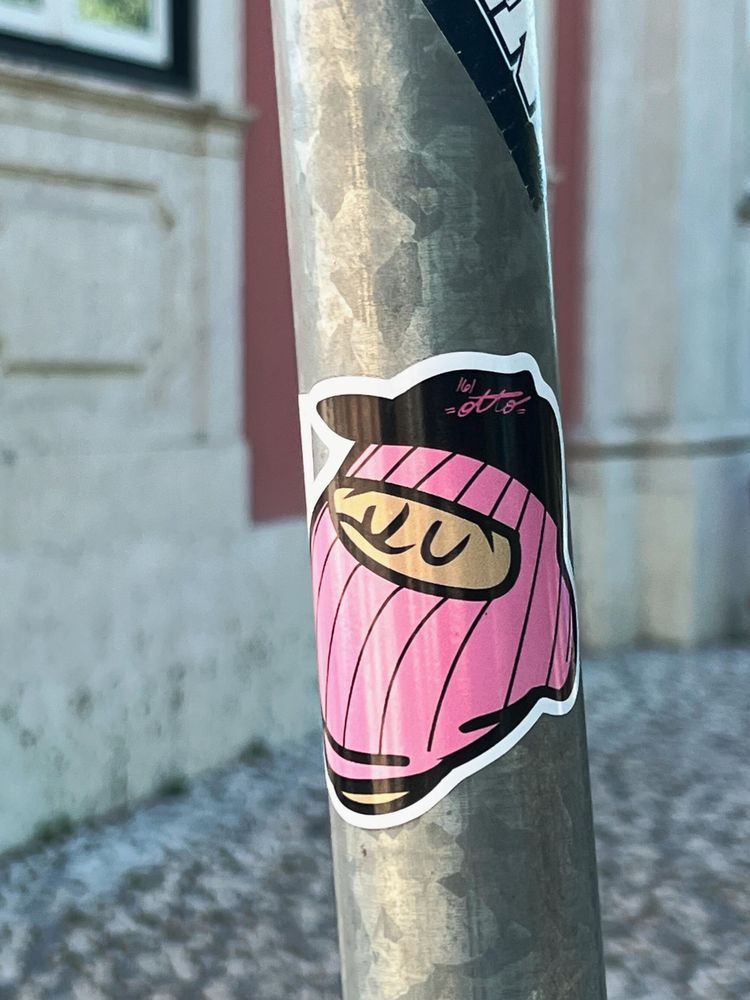 Sticker on a utility pole. A sleepy man, wearing a pink balaclava, and a black hat. 