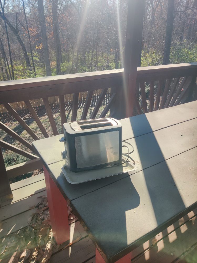 Remains of toaster after receiving the close embrace of a fire blanket and spray of a fire extinguisher. On a outdoor table with trees calmly watching in the background.