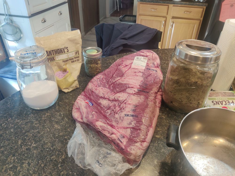 Picture of pickling salt, pink curing salt, brown sugar, pickling spice blend, & a large brisket. The pan in the picture is what I used to heat up the brine.