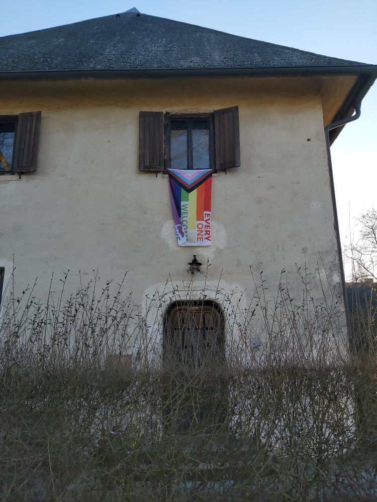 Aus dem Fenster eines zweistöckigen Hauses hängt eine Regenbogenfahne auf der steht: 