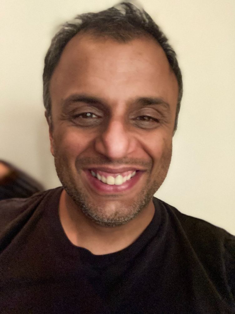 Photo of head and shoulders of Sandip Patel, wearing a dark T shirt, against a cream background