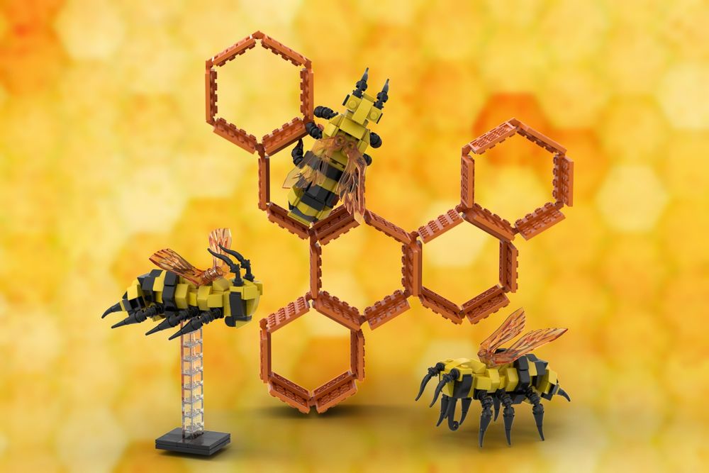 Prototype LEGO bees and honeycomb showing 3 bees, each having a yellow body with black stripe, black, articulated legs, black antennae and mouth parts and amber wings.  One bee (left, foreground) is on a clear plastic LEGO plinth; a second bee (left of centre) is facing away from us on the an upper hexagon of a 6-hexagon, amber LEGO honeycomb (shaped roughly in a Y-formation, tilted slightly to the right); and the 3rd been on the 'ground', facing left, to the right side of the 'honeycomb'.  All against a yellow/amber background having feint hexagon watermarks all over. (phew!)  