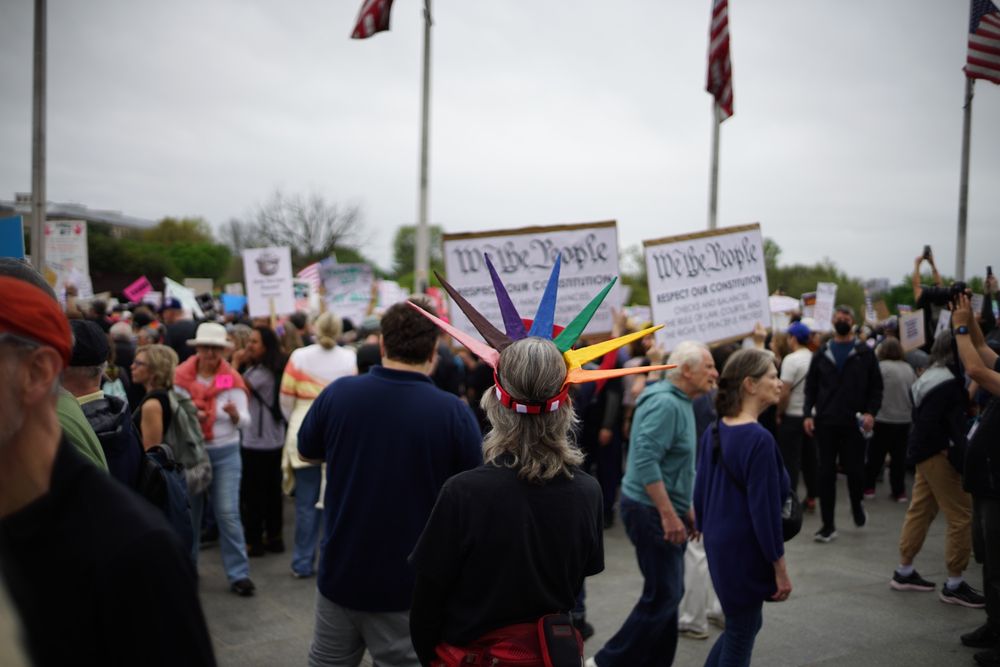 A person wearing an LGBTQIA+ rainbow colored crown in the style of the Statue of Liberty 