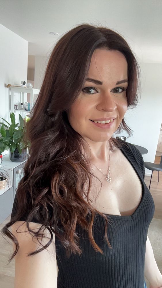 A selfie of me showing off my new hair. I had 3 packs of extensions added to my hair to make it thicker and fuller. The hair is very deep brown with a hint of red, and curled. 