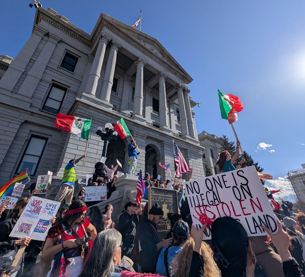 Protesters holding signs at a rally in Denver opposed to DOGE activities and Trump's Executive Orders. 