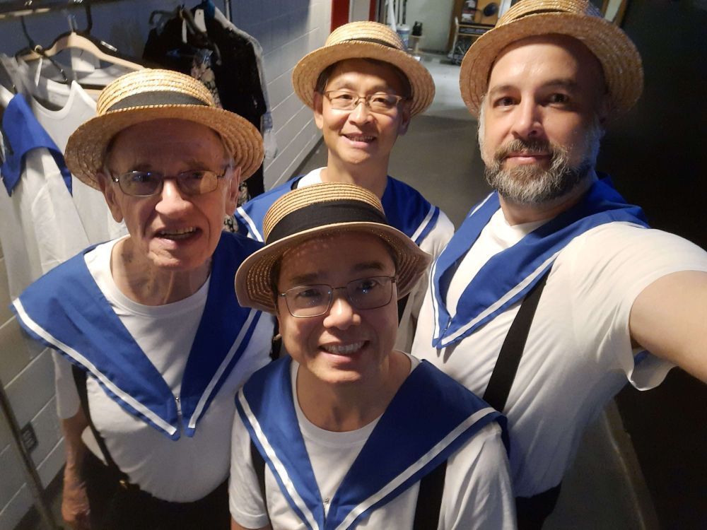 Four members of the men's chorus of HMS Pinafore backstage, dressed as sailors taking a selfie from high up.