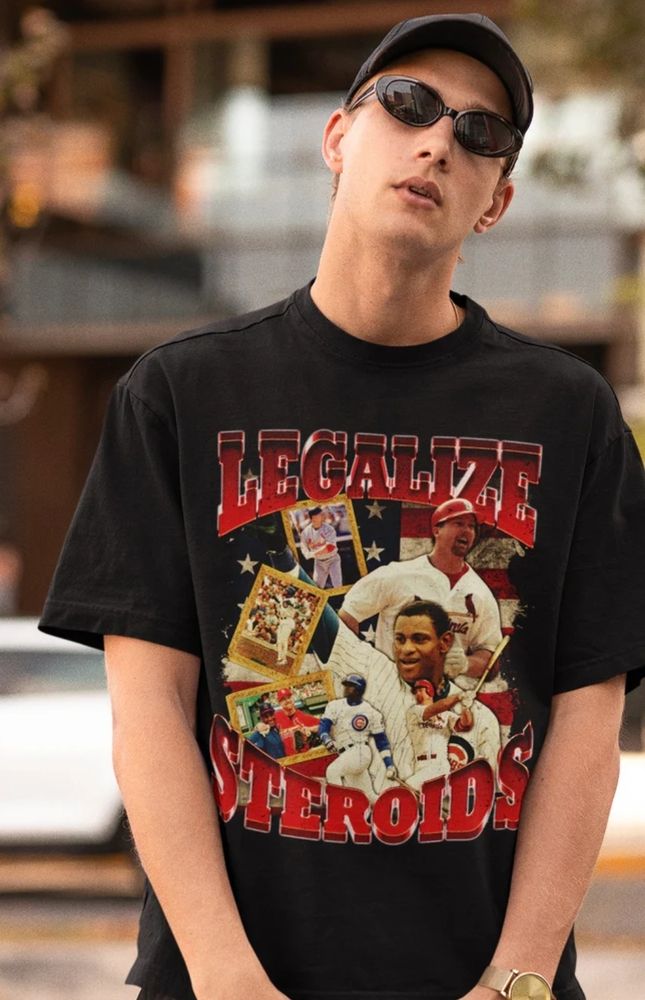 lanky pale white dude with a baseball cap and shades standing on a city street. he is wearing a black t shirt featuring baseball players and the words LEGALIZE STEROIDS emblazoned on the top and bottom.