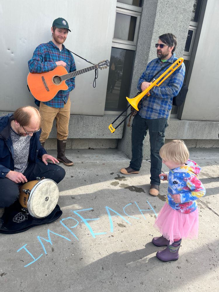 Child watches band with the word impeach written in sidewalk chalk in front of them 