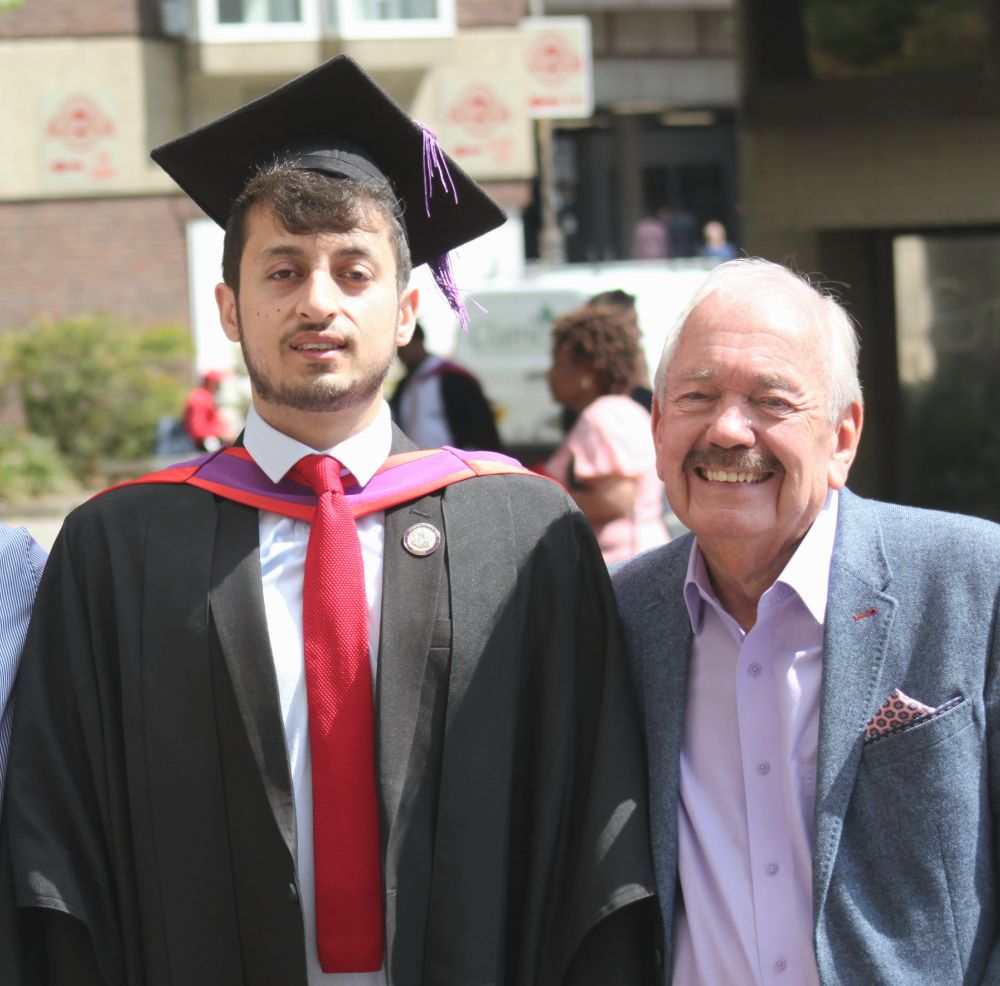 A photo of 2 men, one wearing graduation attire