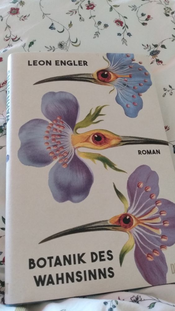 Buch "Botanik des Wahnsinns' auf geblümter Bettdecke liegend