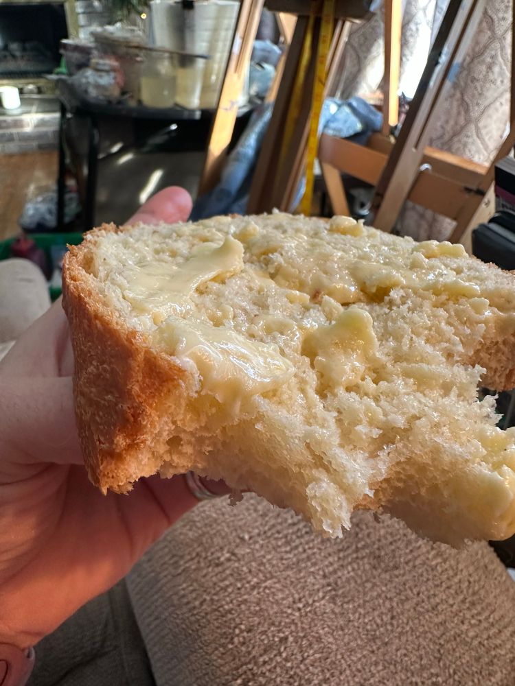 A soft billowy slice of freah baked buttered bread with bites out of it.