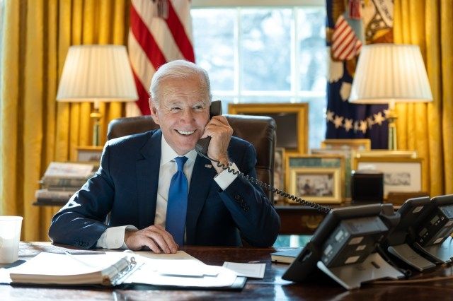 Joe Biden at his desk smiling while talking on the phone