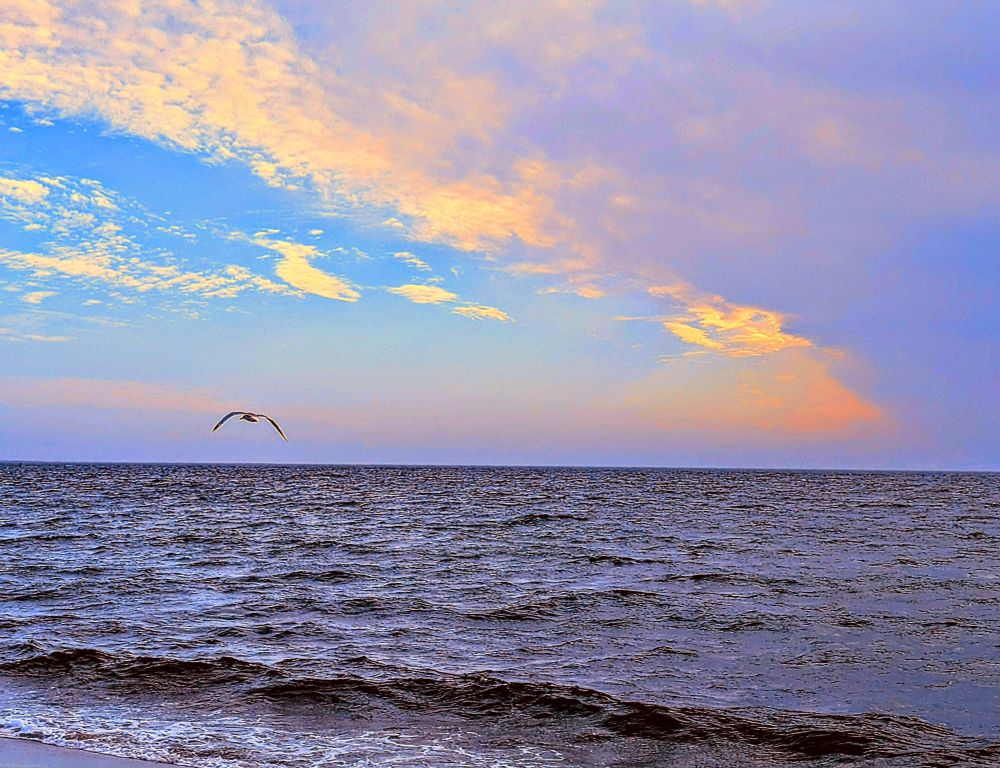 I see golf lying over the water clouds colored by the setting Sun waves coming in