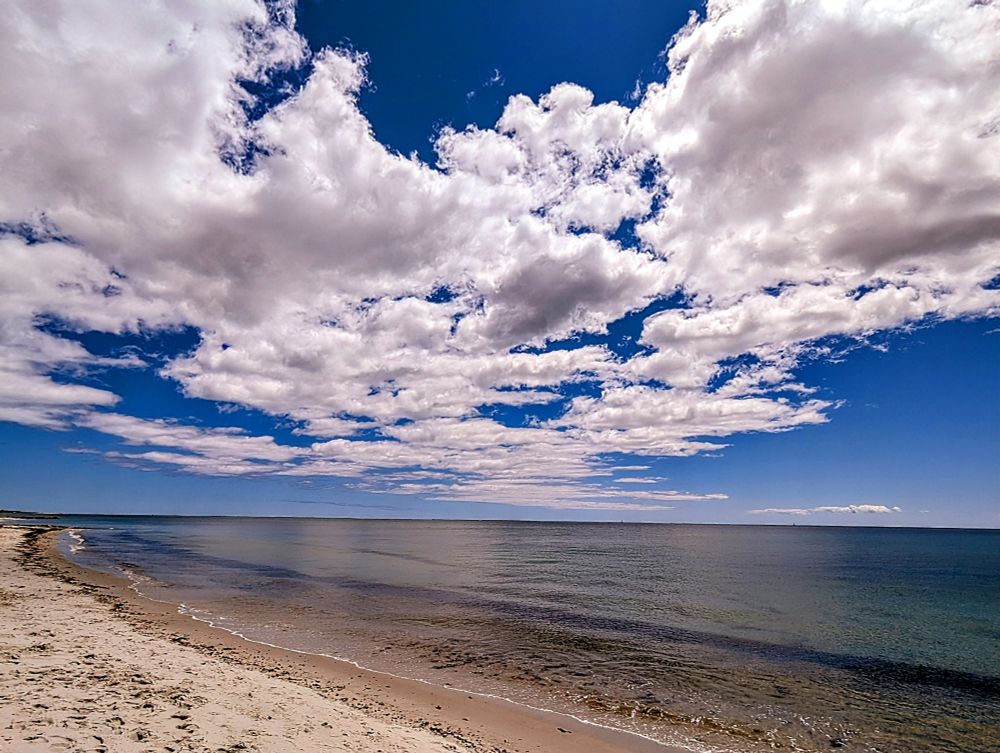 The calm ocean, sand on the left, cloudscape above