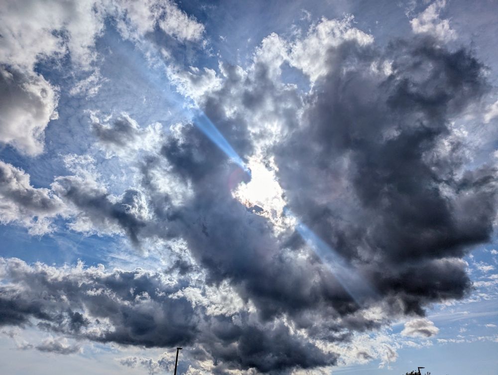 A dark cloud with the sun in center, light coming out In beams, blue around it
