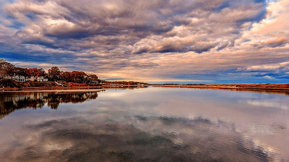 Clouds above the York River a slight reflection in the water reflections from the trees on the left land centering the photo blue showing in between the stormy clouds