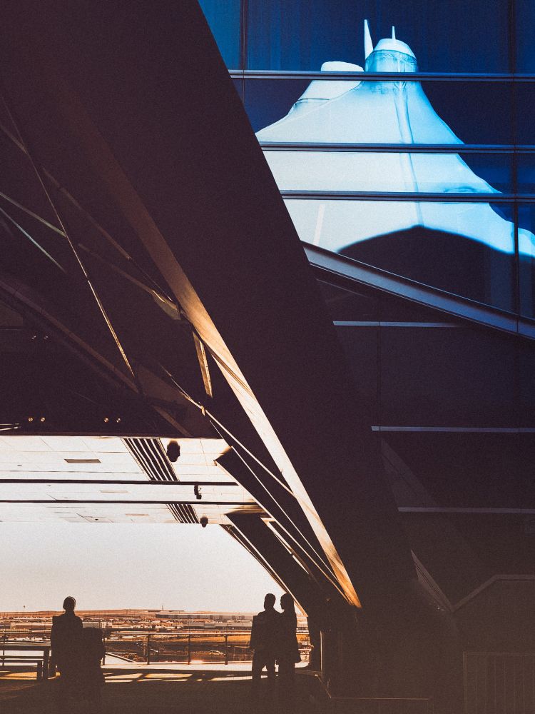 The white tents of Denver International Airport are reflected in the windows of the adjacent hotel. In the shadows are a single traveler and a pair of Jehovah Witness enthusiasts.