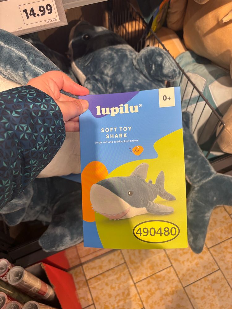 A lupilu-branded cardboard tag attaxhed to blue and white shark plushie in a Lidl that resembles the blåhaj shark plush from IKEA.