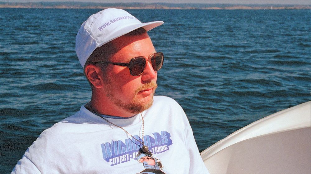 Jag med keps och solglasögon lutad mot relingen i en båt ute på havet. 