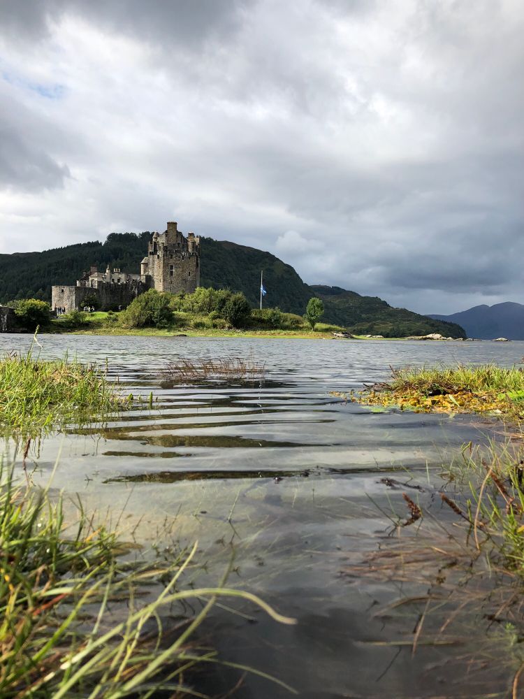 View of Eilean Donan, a castle on an island in the middle of a loch, with water in the foreground