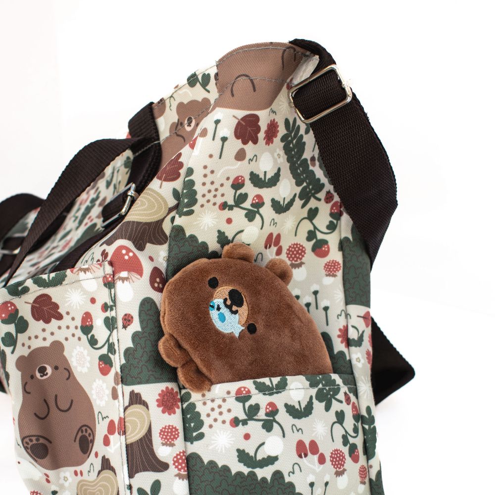 photograph of a cute, brown bear coin purse inside the pocket of a tote bag with bears, mushrooms, strawberries, and other natural elements. 