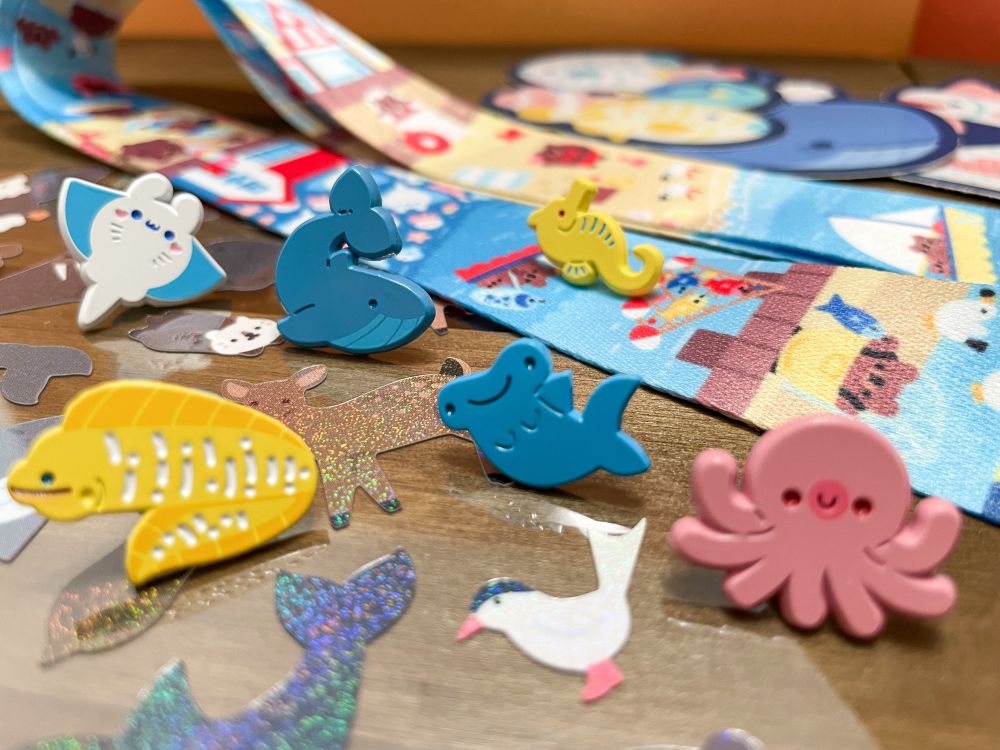 Photograph of enamel pins, stickers, and lanyards all with a seaside or ocean theme. 