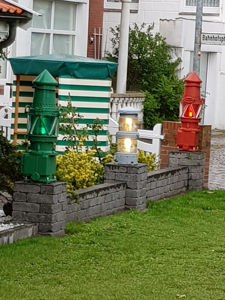 Auf einer Mauer stehen auf jedem der drei Pfeiler ein beleuchteter Leuchtturm zur Dekoration. Der links ist grün , in der Mitte ist weiß,  der rechts ist rot.