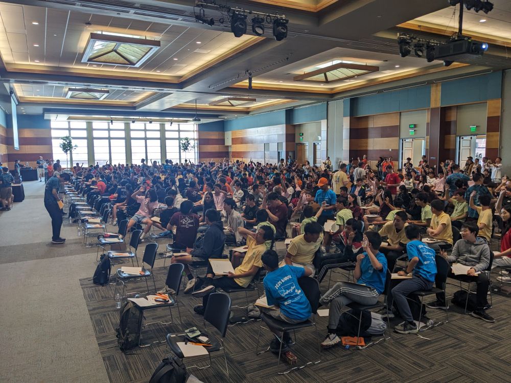 A lot of students sitting in chairs doing math in a ballroom