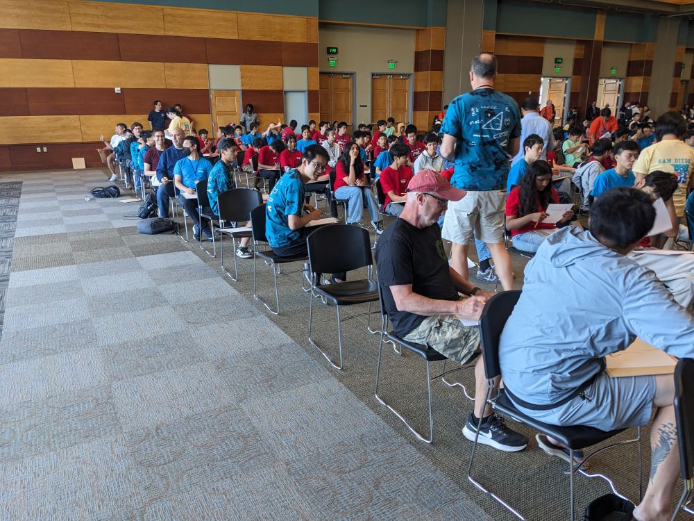 Various math team coaches seated one behind the other, preparing to compete against their students. 