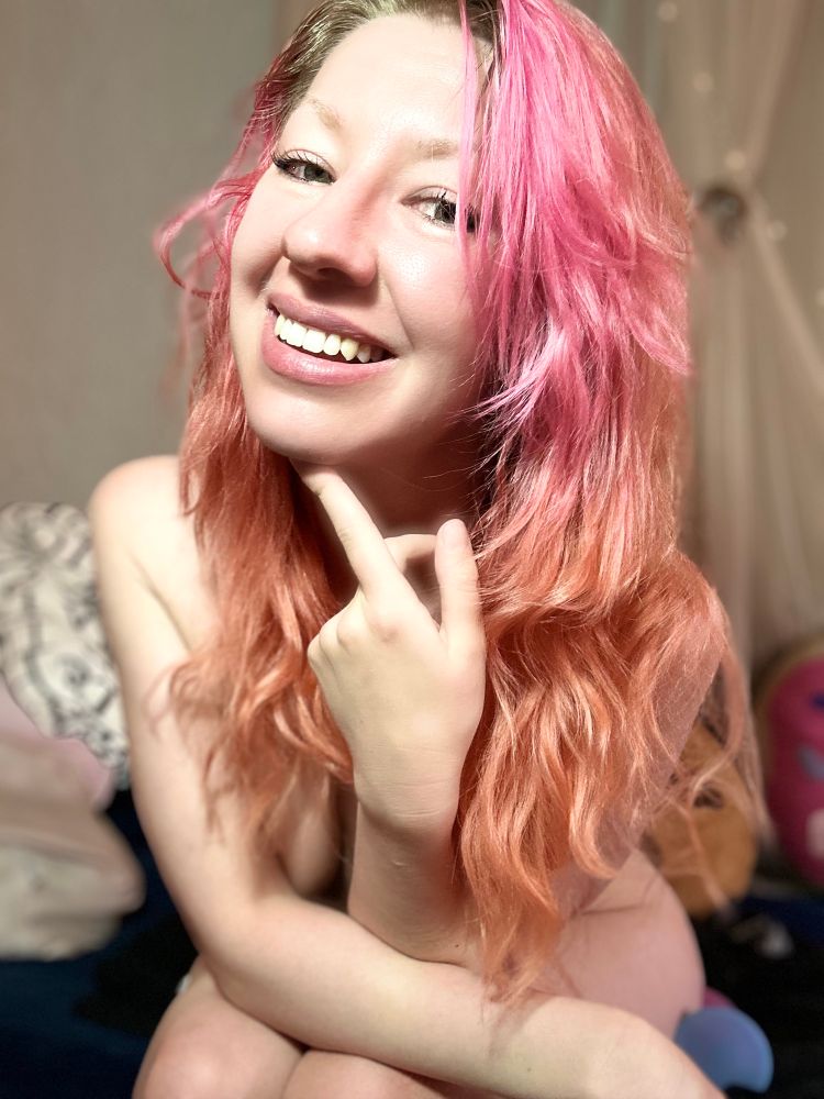 Valentine smiling at camera with finger to chin, implied nude
