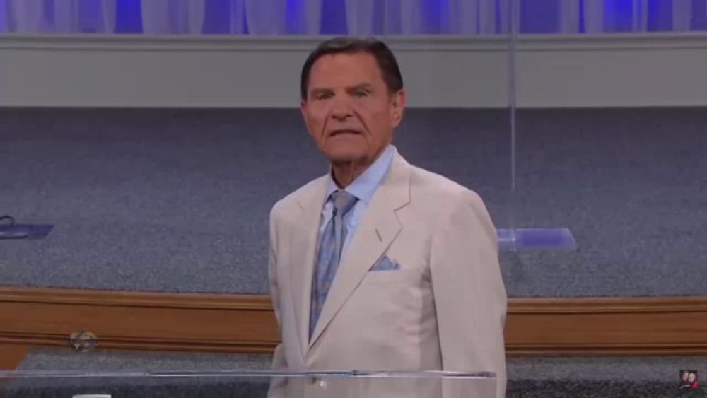 a man in a white suit and blue tie stands behind a clear podium