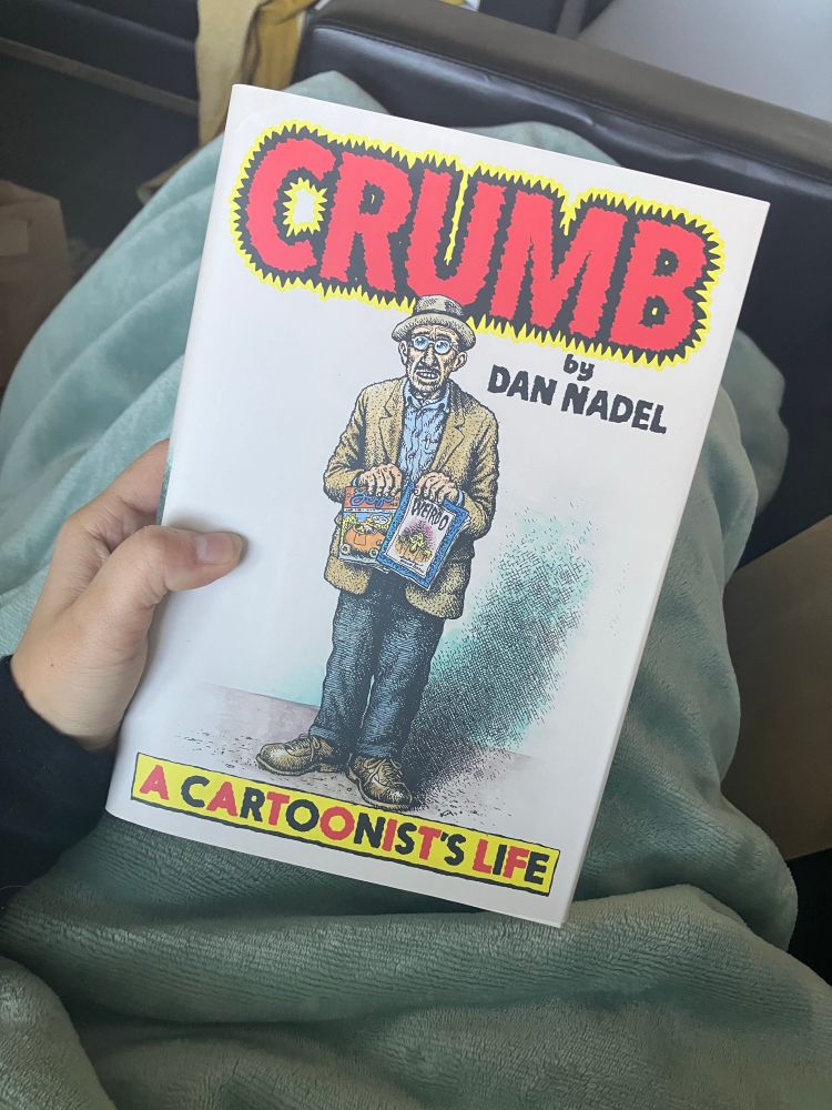 A hand holding the Crumb biography by Dan Nadel. The cover features an illustration of Crumb with the subtitle “A Cartoonist’s Life” at the bottom of the cover. 