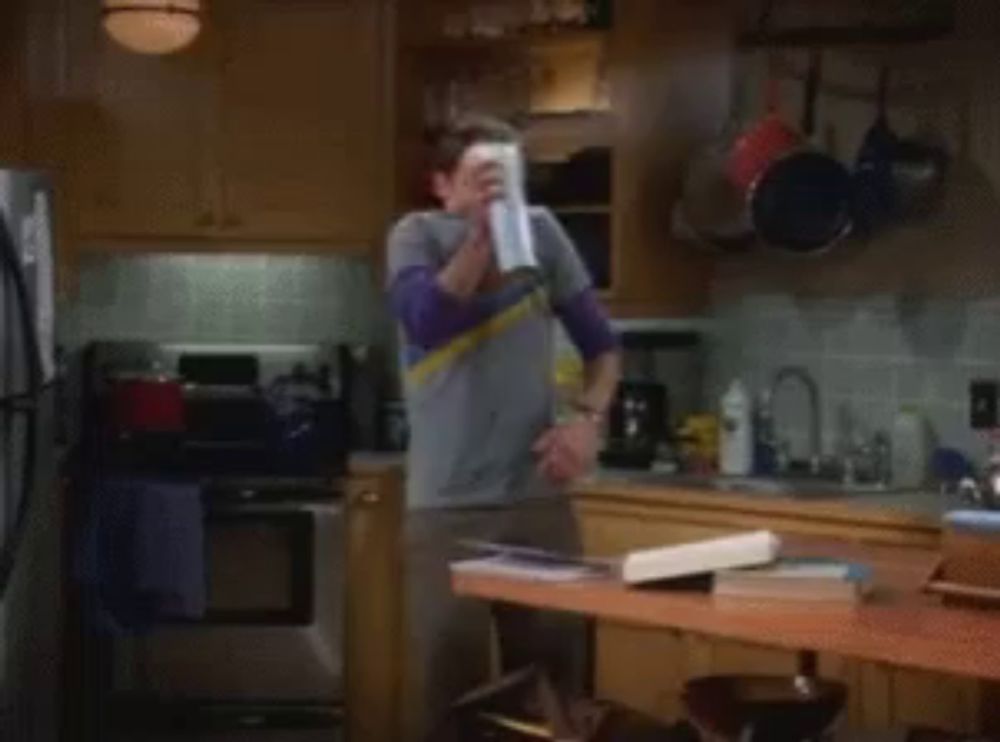 a man in a gray shirt is spraying a can of air freshener in a kitchen