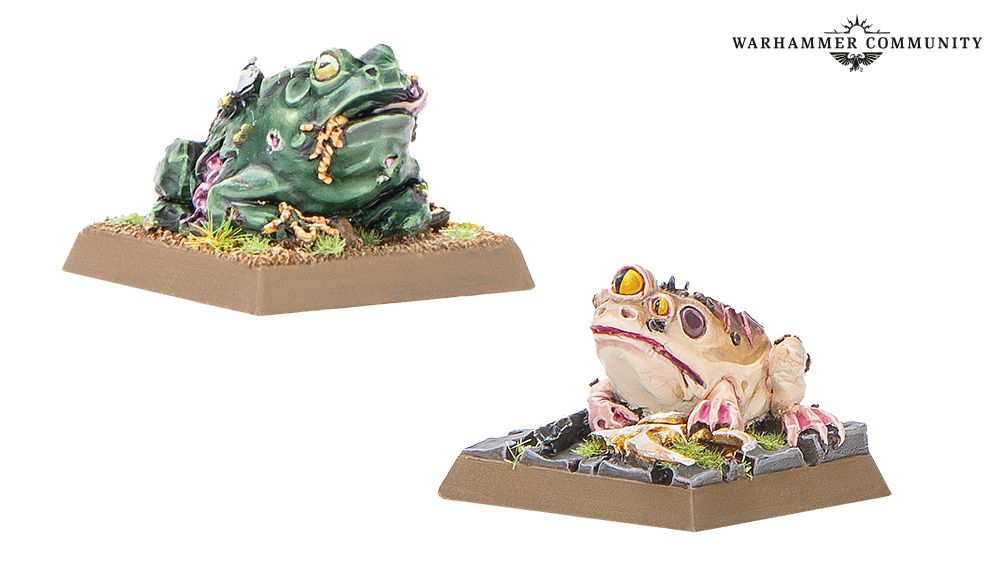 Two miniature fronts on bases, one with green skin and exposed flesh on its righg and the other with a paler skin, brown spots, and three eyes.