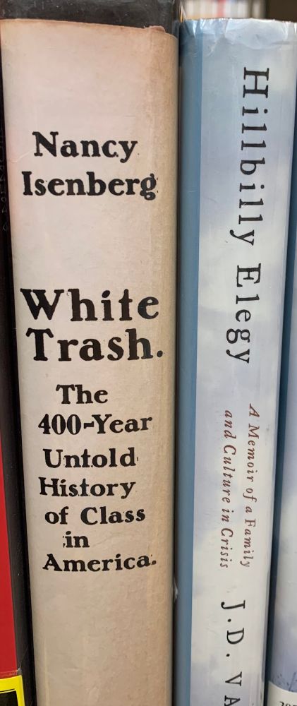 The spines of two books next to each other on a library shelf. On the left, “White Trash: The 400-Year Untold History of Class in America,” and on the right, JD Vance’s memoir,“Hillbilly Elegy”.