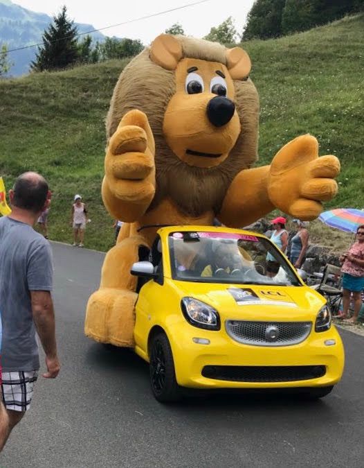 Huge lion on the back of a small yellow LCL car ascending the Col du Colombier as part of the Tour de France caravan. 