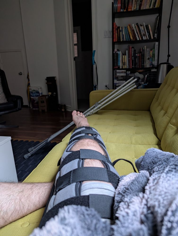 Poster's right leg in a full-leg brace while lying on a couch, crutches behind 