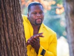 Man in a yellow suit behind a tree looks on with eager anticipation.