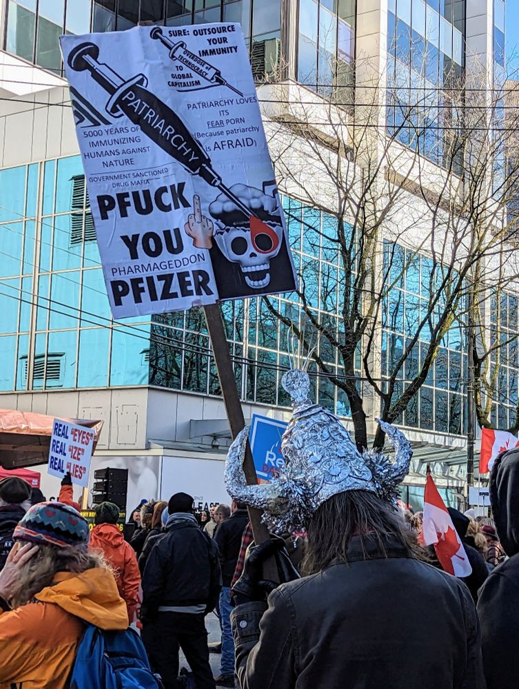 Photo from a Freedom Convoy rally in February 2023 in downtown Vancouver. A man wearing a tinfoil shaped into a viking helmet holds a sign that says "phuck you pfizer"