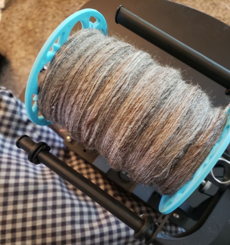 An up close picture of single ply handspun yarn on an e-spinner. The yarn is a natural oatmeal colored BFL wool, pretty rustic looking, spun at about a fingering/sport weight.