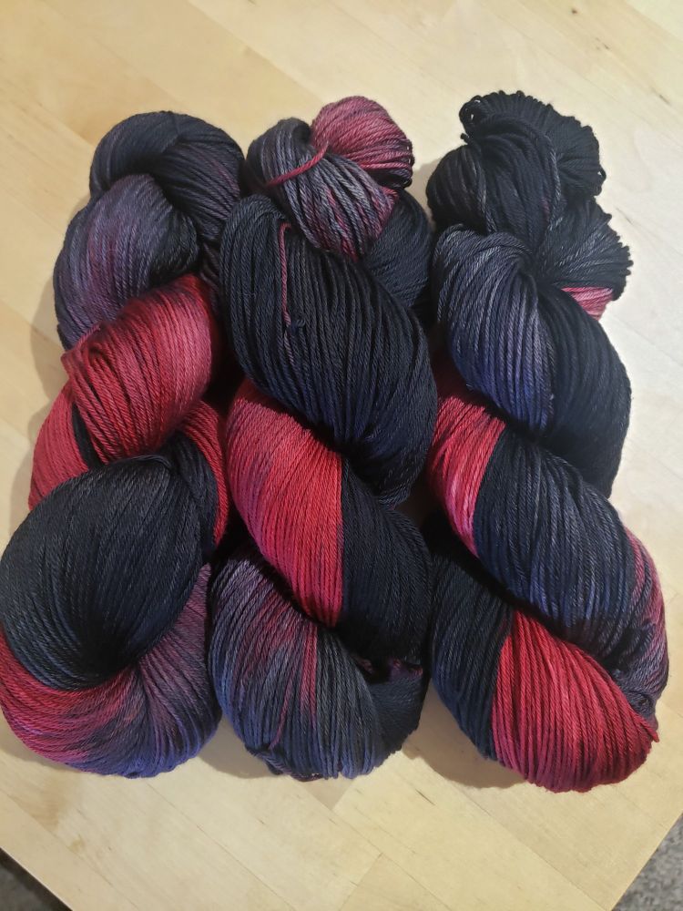 Three hanks of yarn on a table. Each one is about 60% solid black, which fades into grey and then a deep red color.